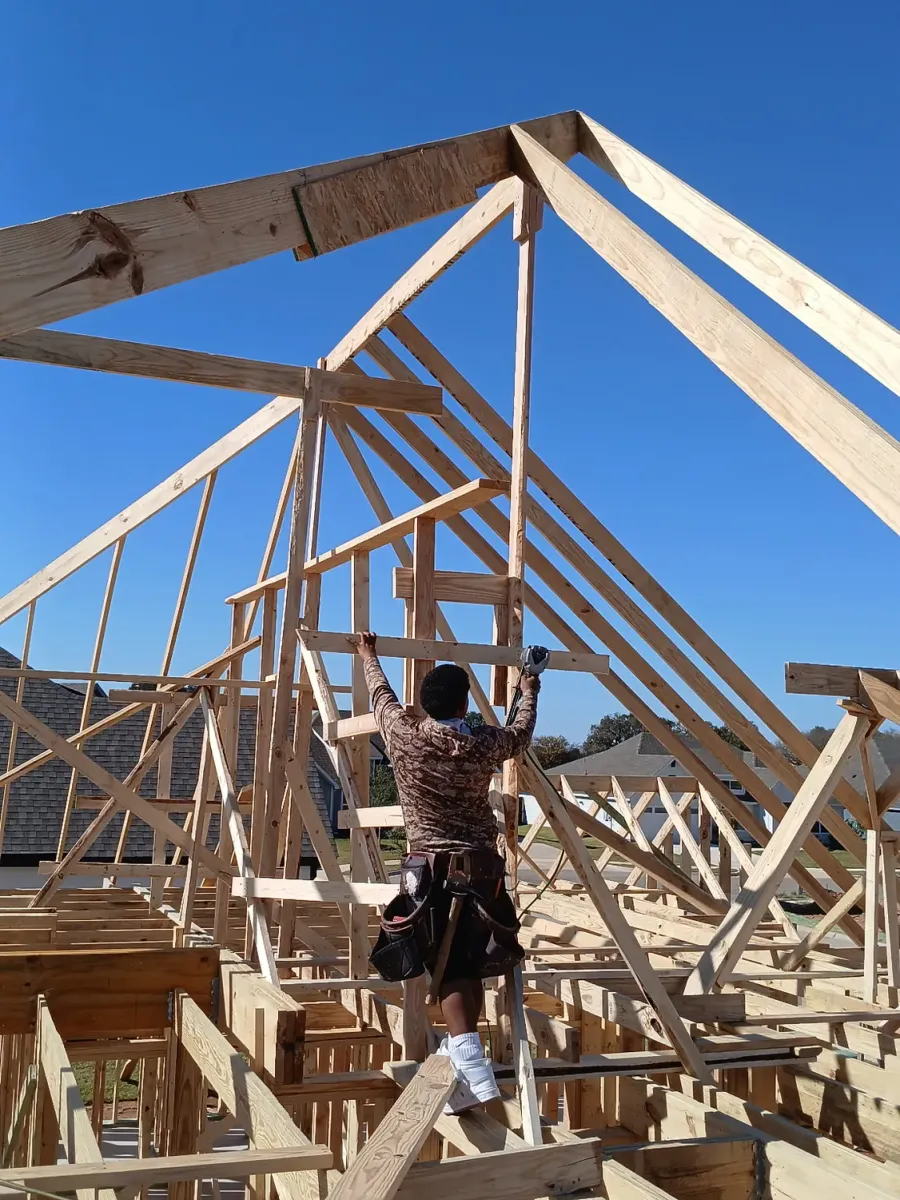 Carpenter nailing off roof trusses on a new house frame under a clear sky